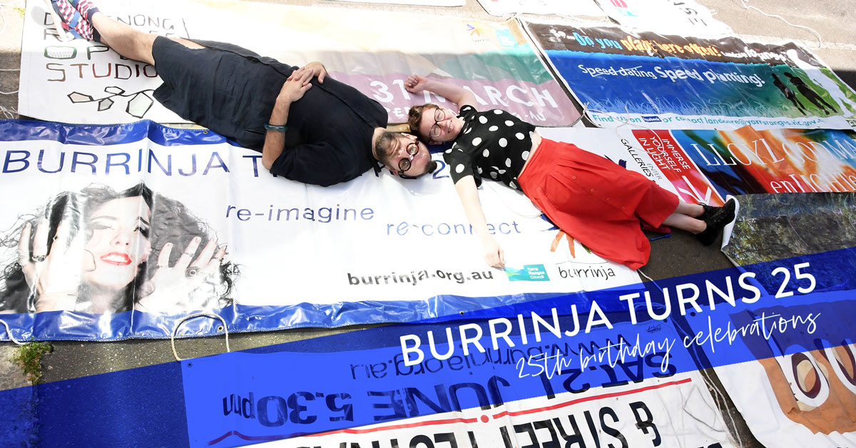 Burrinja Birthday 25th Birthday Celebrations. Two people lie diagnally with their heads together across old vinyl banners